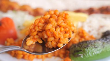 Bir kaşığın üzerinde bulgur pilavının arka plandaki diğer tabaklarla yakın çekimi..