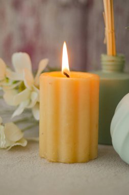 Beyaz çiçeklerin yanında titreyen bir mum ve yeşil bir vazo ambiyansı belirler..