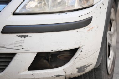 Beyaz bir araba ön tamponunda görünür çizikler ve göçükler gösteriyor..