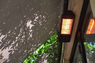 Güneş ışığı, yeşillik çerçeveli desenli bir duvara gölge düşürür..