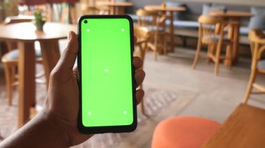 Rahat bir kafede yeşil geçmişi olan bir telefon tutan bir kişi var..