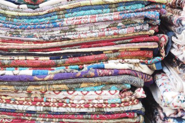 Bolca renkli kumaş yığınları hareketli bir pazar alanını dolduruyor.