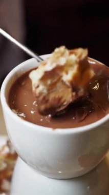 Bir insan bir parça pastayı zengin bir çikolataya batırır. 