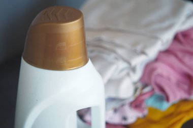 Bir şişe çamaşır deterjanı düzgünce yerleştirilmiş kıyafetlerin yanında duruyor..