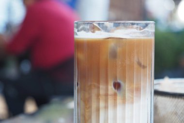 Uzun bir bardak buzlu kahve, açık havada canlı bir masada oturuyor..