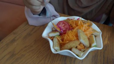 Bir el çatal tutar, taze salatayı çıtır tavukla karıştırır..