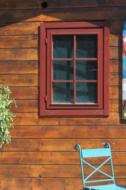 Büyüleyici ahşap bir duvarın yanında kırmızı bir pencere ve mavi bir sandalye var..
