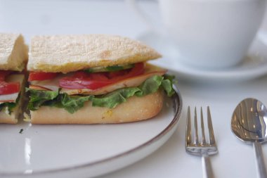 Marul, domates ve hindiyle dolu lezzetli bir sandviç çayın yanına oturur..