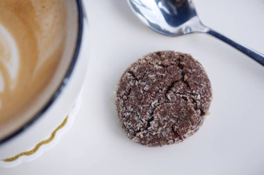 Bir çikolatalı kurabiye beyaz bir yüzeyde bir fincan kahvenin yanında dinlenir..