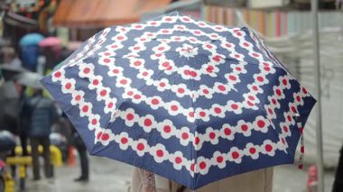 Kalabalık yağmurlu bir günde renkli şemsiyelerle kalabalık bir pazarda geziniyor..