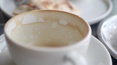 Sıcak bir fincan kahve bitmek üzere, boş tabaklarla çevrili..