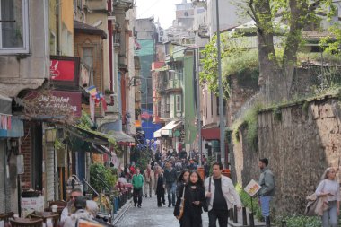 Kalabalık, dükkanlar ve kafelerle dolu hareketli bir sokakta yürüyor..