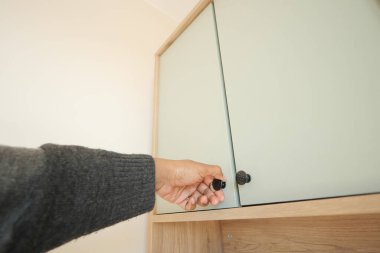 Bir el, iyi aydınlatılmış bir odada dolap sapına uzanıyor..