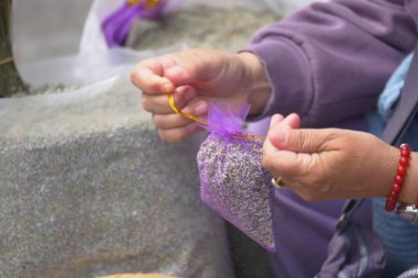 Bir insan kalabalık bir pazarda lavanta kesesini özenle sarar..