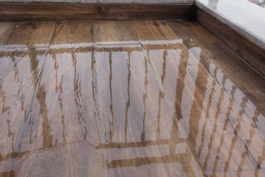 Yağmur damlaları ahşap zeminde su birikintileri oluşturur, yansımaları gösterir.