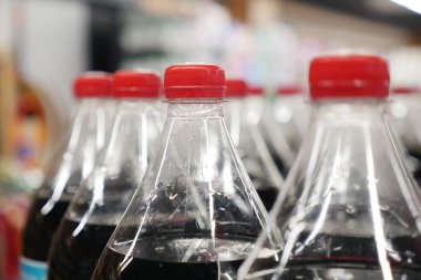 Mağaza koridorunda kırmızı şapkalı siyah soda şişeleri..