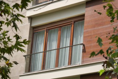 Ahşap aksanlı, akıcı perdeli ve ağaçlı büyüleyici bir balkon..