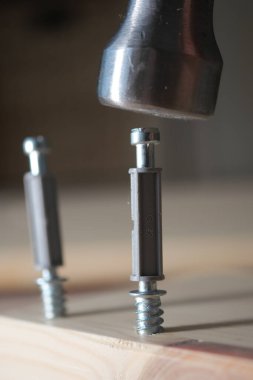 Bir çekiç tahtaya saplanmış bir vidaya vurmak üzere..