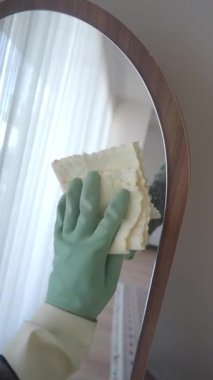 Bir insan yeşil eldiven giyerken aynayı bezle temizler..