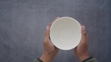 Bir insan, iki eli de hafif beyaz bir kase tutar..