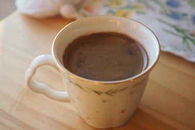 Sıcak bir fincan sıcak çikolata ahşap bir masanın üzerinde duruyor, sıcaklığı davet ediyor..