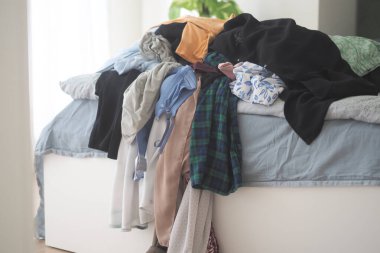 Giysiler bir yatağa saçılmış, bu da sabah atmosferini bozuyor..