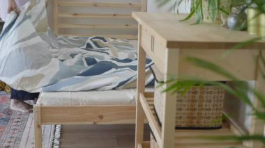 Parlak bir odada, ahşap bir yatakta yorgan hazırlayan biri..