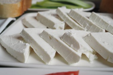 Dilimlenmiş taze peynir parçaları beyaz bir tabakta düzgünce dizilmiş..