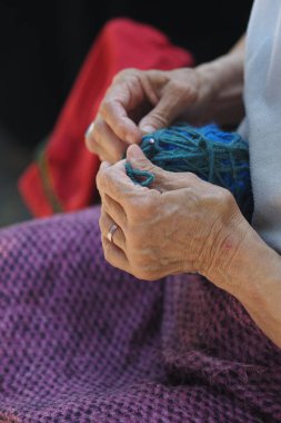 Eller dışarıda otururken ustalıkla renkli iplikler dokuyor..