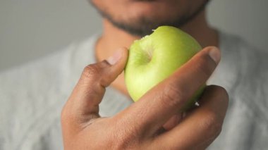 Bir insan taze yeşil bir elmayı sıkıca tutarken tadıyor..