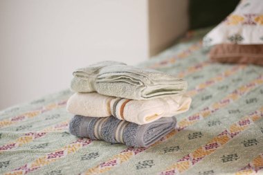 Yeni katlanmış havlular sıcak bir odadaki rahat ve desenli bir yatak örtüsünün üzerinde dinleniyor..