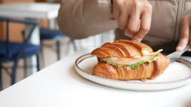 Bir insan taze malzemelerle dolu bir kruvasan sandviçin tadını çıkarmaya hazırlanır..