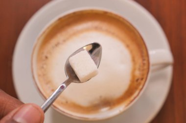 Bir kaşık dolusu şekeri köpüklü kahvenin üstünde tutan el..