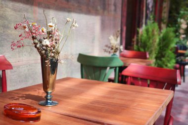 Küçük bir açık kafe masasında çiçekli bir vazo ve bir kül tablası sergilenir..