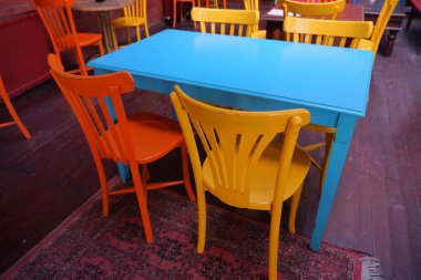 Parlak turuncu ve sarı sandalyeler hayat dolu bir kafede mavi bir masayı çevrelemiş..