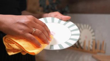 Bir insan sıcak bir mutfak ortamında sarı bir bez kullanarak tabağı siler..