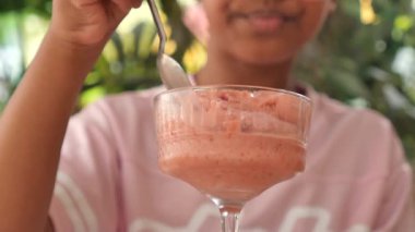 Genç bir kız dışarıda otururken kremalı çilekli tatlının tadını çıkarıyor..