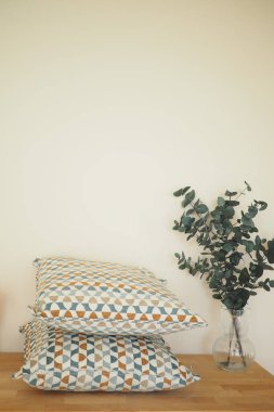 İki desenli yastık okaliptüs vazosunun yanındaki ahşap bir masada dinleniyor..