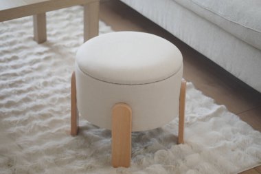 Yumuşak kumaşlı yuvarlak bir şilte koltuğun yanındaki yumuşak bir halıya oturur..