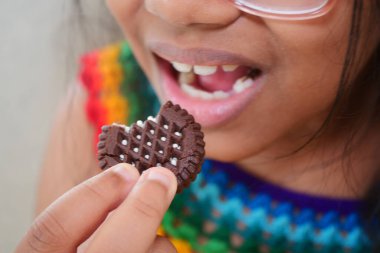 Bir çocuk gülümserken çikolatalı kurabiyeden bir ısırık alır..