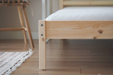 Parlak bir odada ahşap bir yatak çerçevesi, minimalizm ve basitlik sergileniyor..
