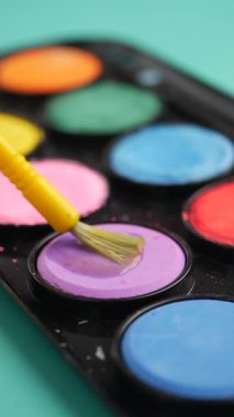 Brush dips into vibrant purple paint in a colorful palette.