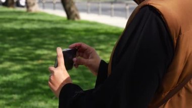 Individual enjoys a sunny day while using a mobile phone outdoors.