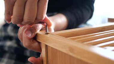 Person uses an Allen wrench to assemble bamboo furniture indoors.