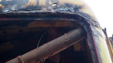 Workers restore a rusty vehicle in a wide outdoor space.
