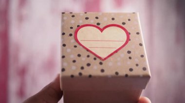 A hand-held gift box features a heart design and polka dots.