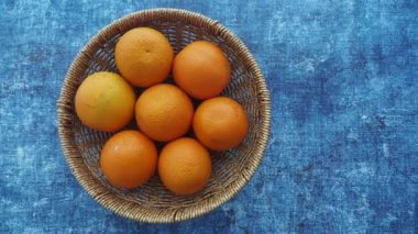 A vibrant basket filled with ripe oranges on a blue surface.