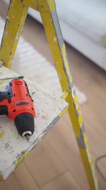 A bright room has a yellow ladder and drill for construction work.