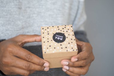 Bir insan üzerinde noktalar ve teşekkür etiketi olan küçük bir hediye kutusu tutar..