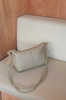 A light gray handbag rests on a wooden bench in a cozy setting.
